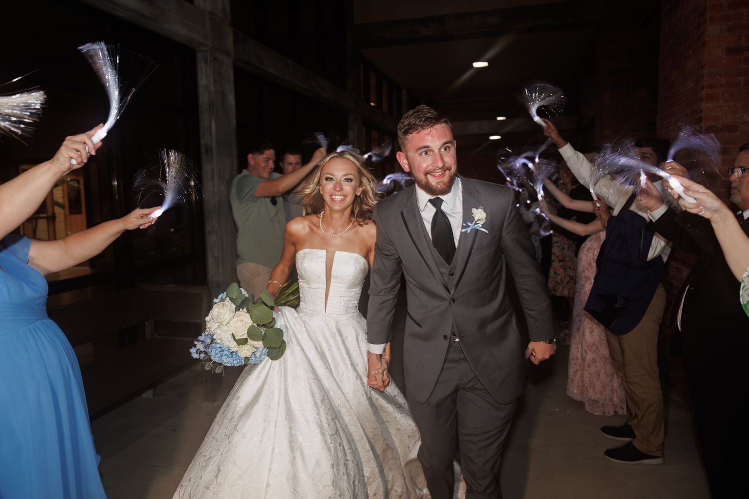 Newlyweds walk through sparkler exit celebration while guests create magical archway of light.