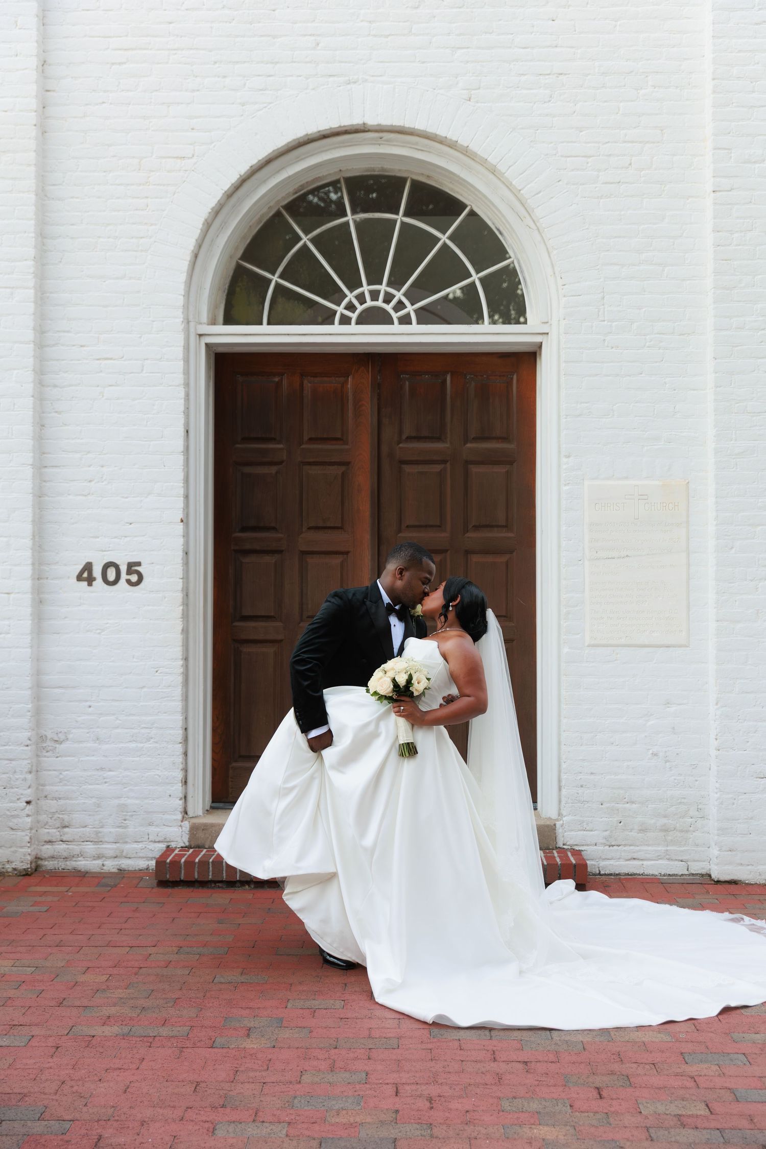 A romantic wedding portrait in front of a grand wooden door with an elegant arched transom window.
