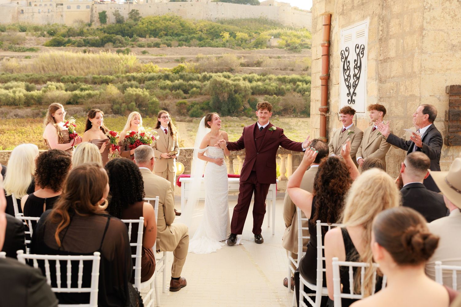 Wedding guests mingle and dance at an outdoor reception venue with stone walls and rustic decor.