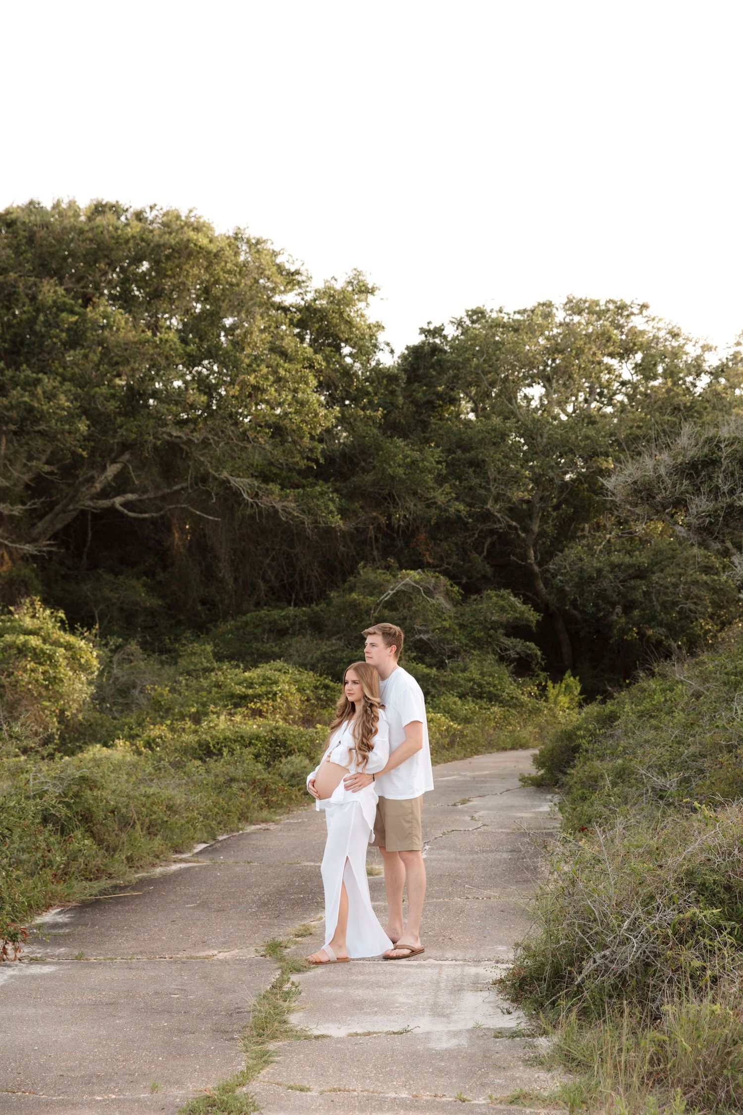Couple in white outfits sharing intimate moments on a nature path surrounded by green foliage.