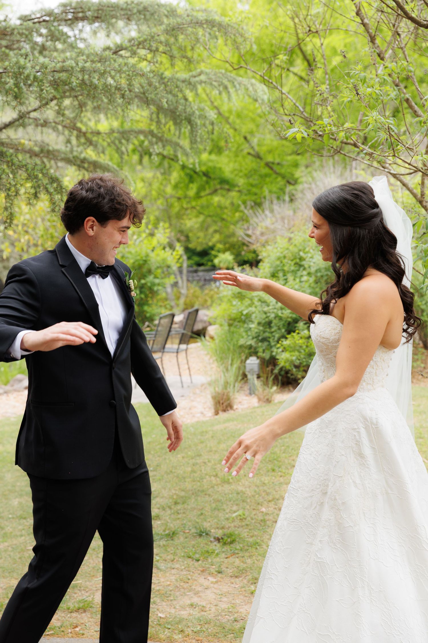 Bride and groom share emotional first look moment reaching toward each other in garden setting.