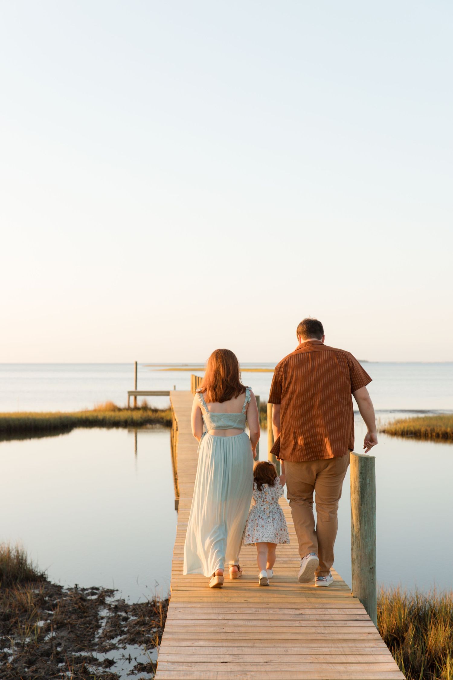 People walking on wooden boardwalk over marsh waters during golden hour.