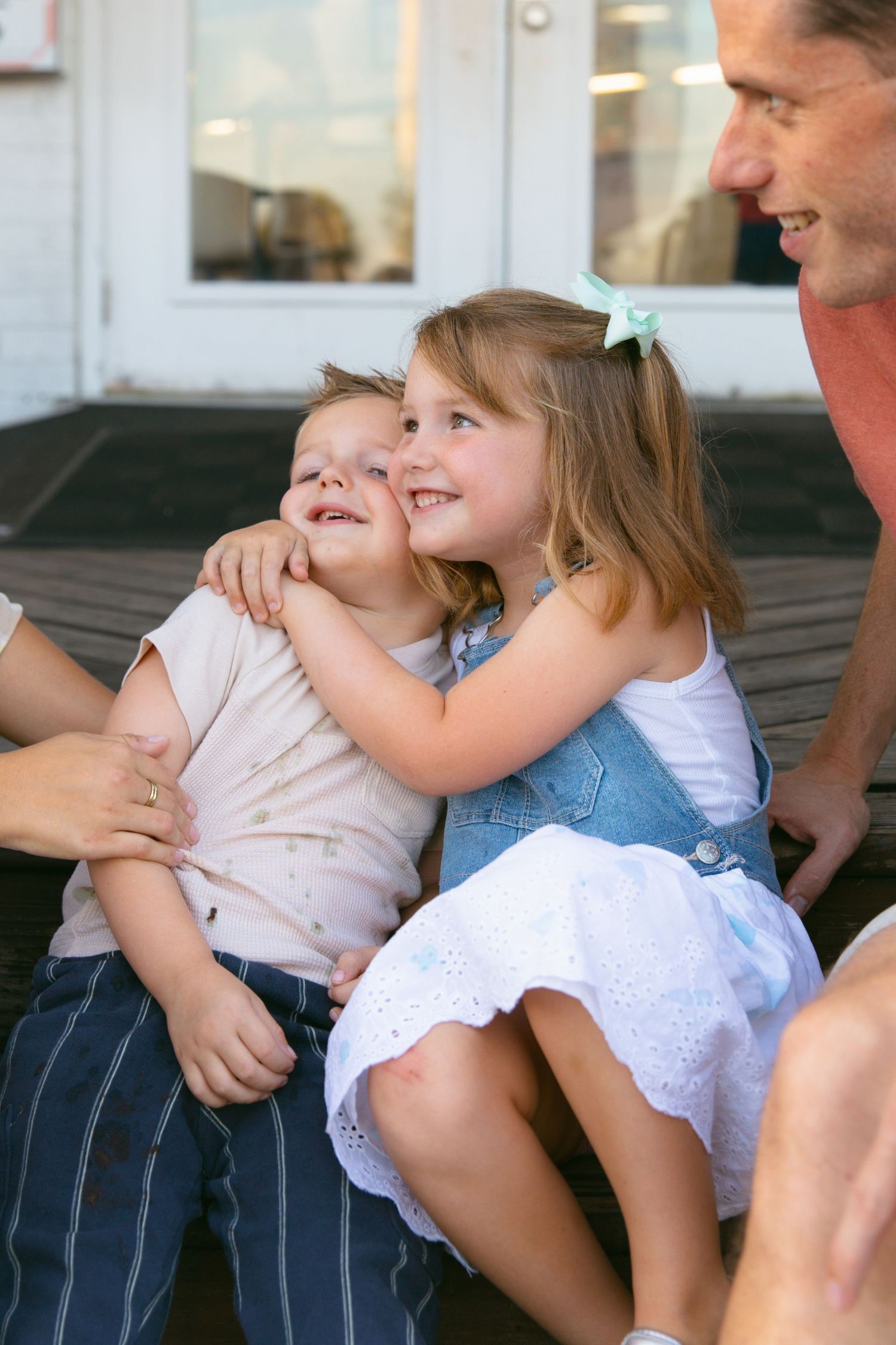 Two children sitting close together and smiling while sharing a sweet moment outdoors.