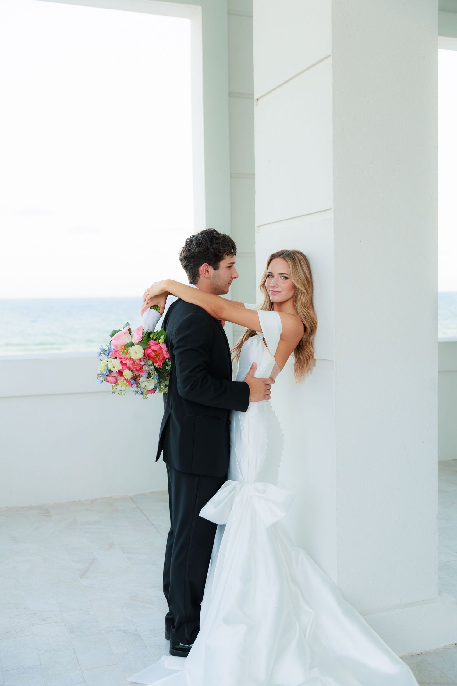 A wedding couple shares an intimate moment on a bright white balcony overlooking the ocean.