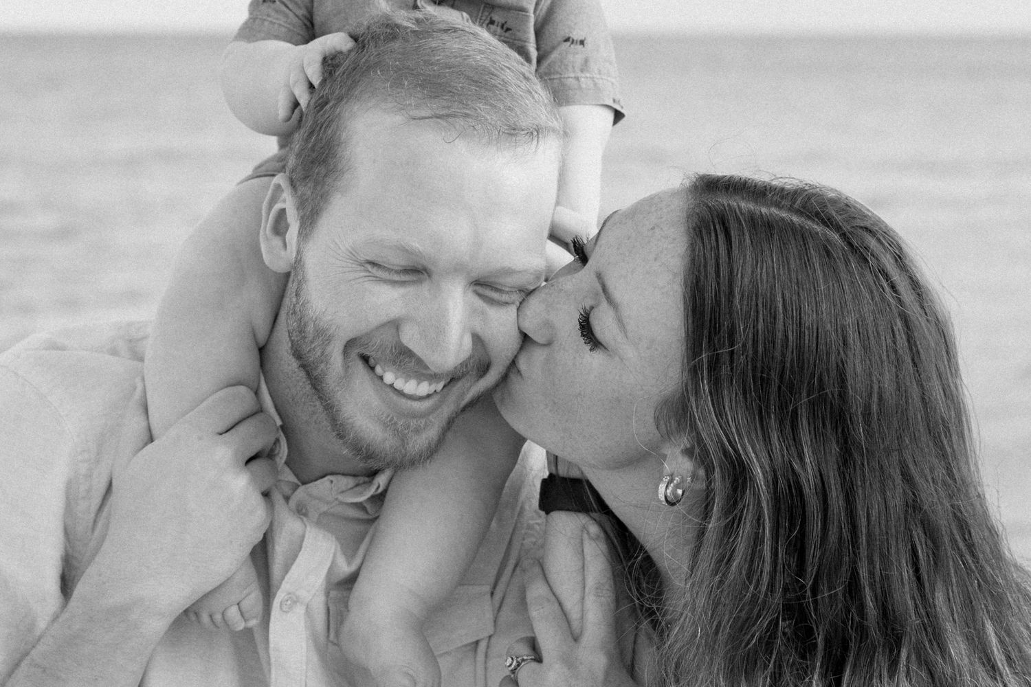 Close up black and white portraits of couple sharing intimate moments on beach boardwalk.