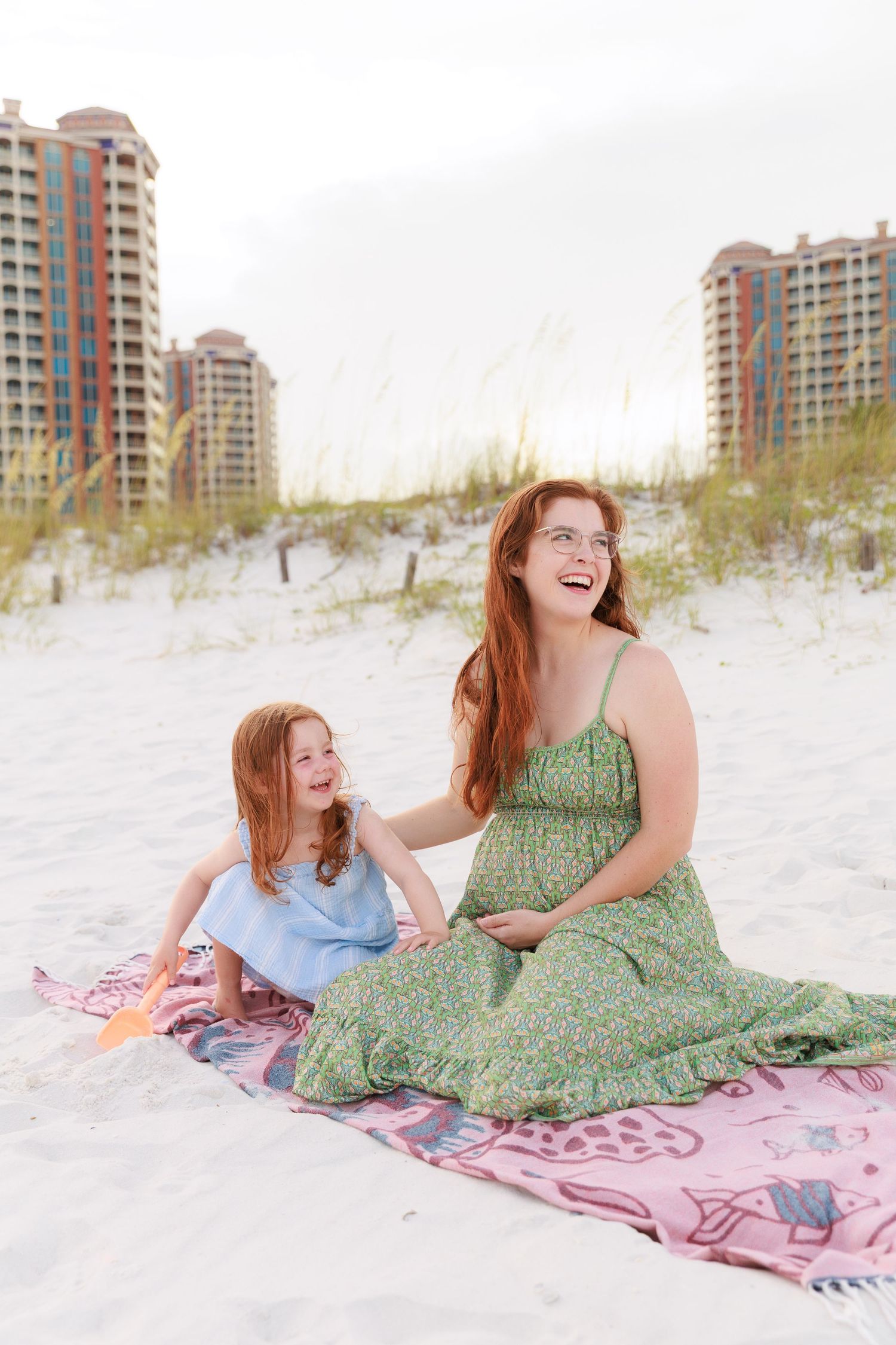 Beachgoers enjoying a sunny day while sitting on a pink blanket with high-rise buildings in the background.