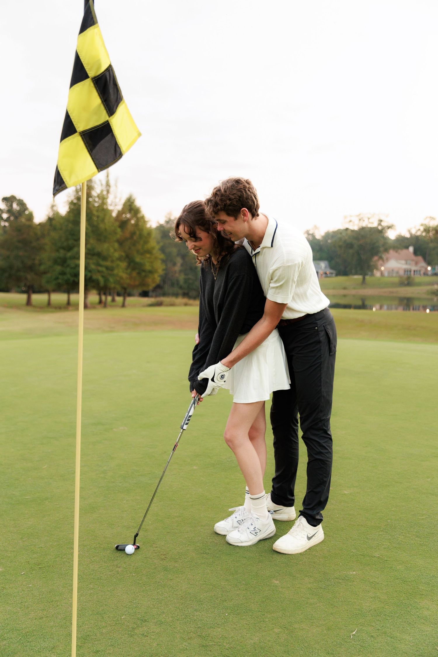 A couple practices putting together on a golf course green with yellow flags in view.