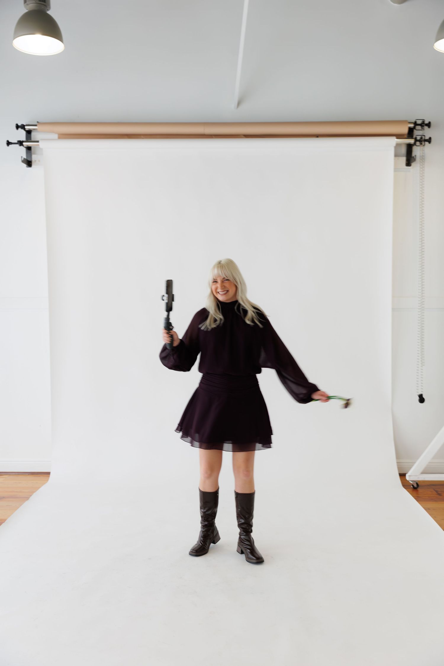 Person in purple dress holding camera while posing against white studio background.