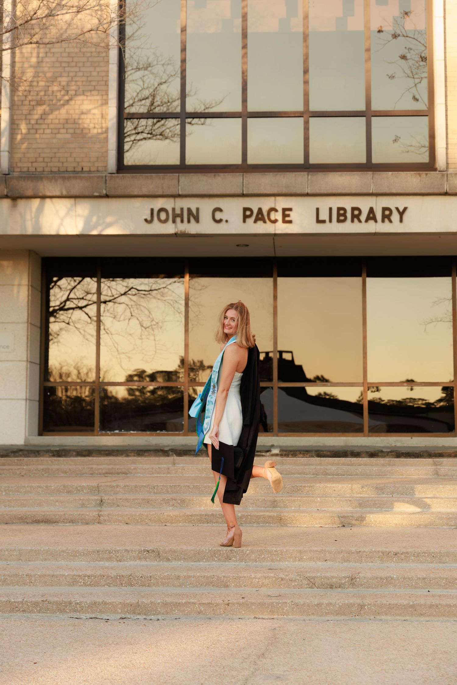 A series of photos showing someone in a graduation gown walking and posing outside the John C. Pace Library at sunset.