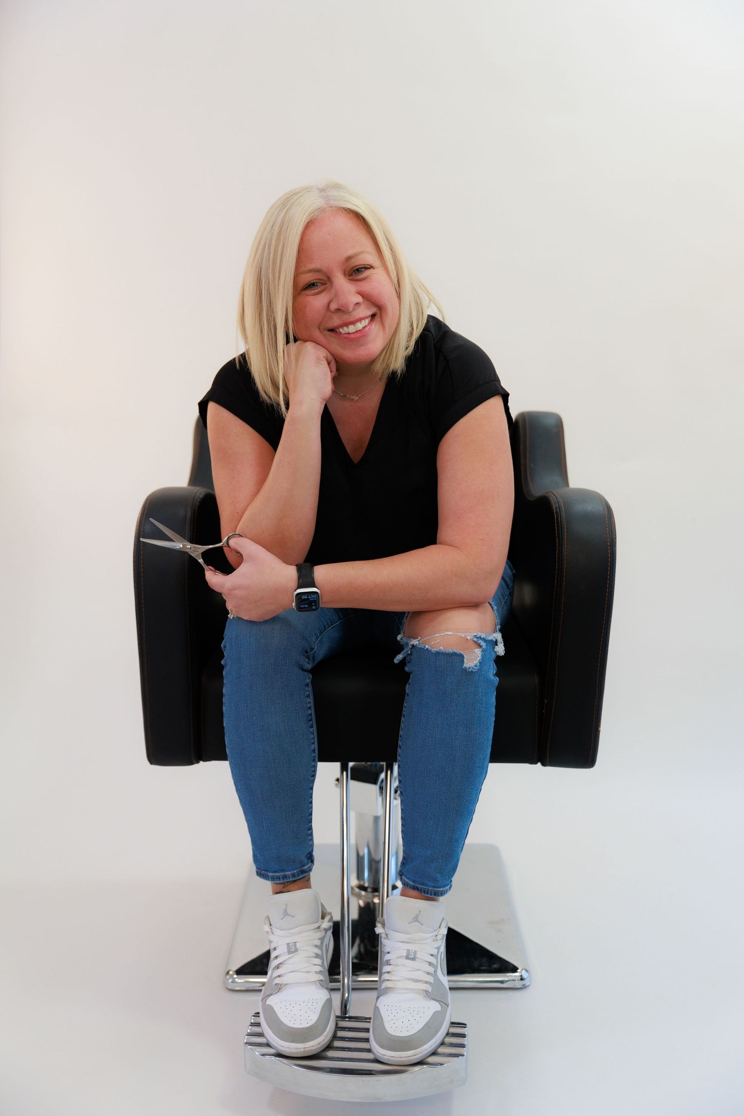 Relaxed pose in salon chair wearing casual black top and distressed denim.