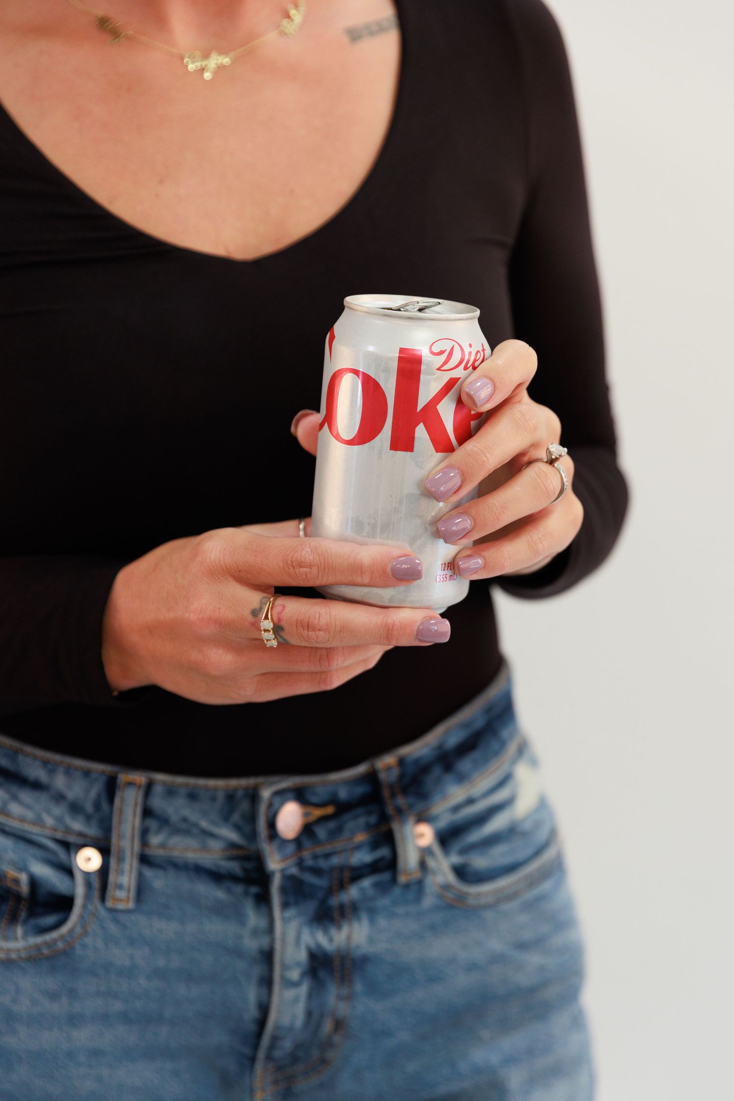 Hand holding Diet Coke can while wearing black top and light wash denim jeans.