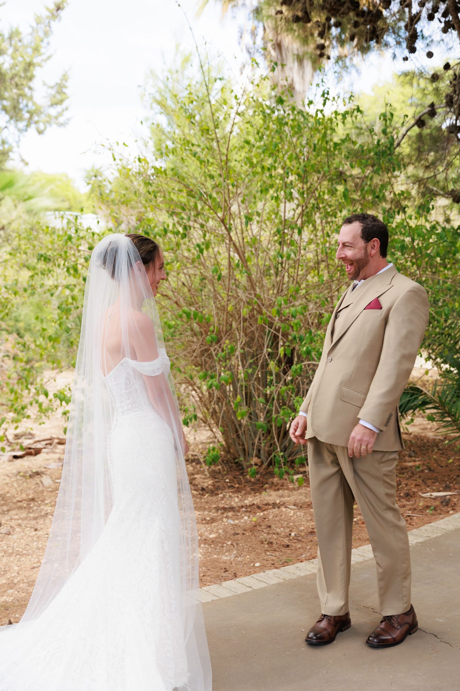 A wedding first look moment captured on a garden path with a bride in white and someone wearing a tan suit.