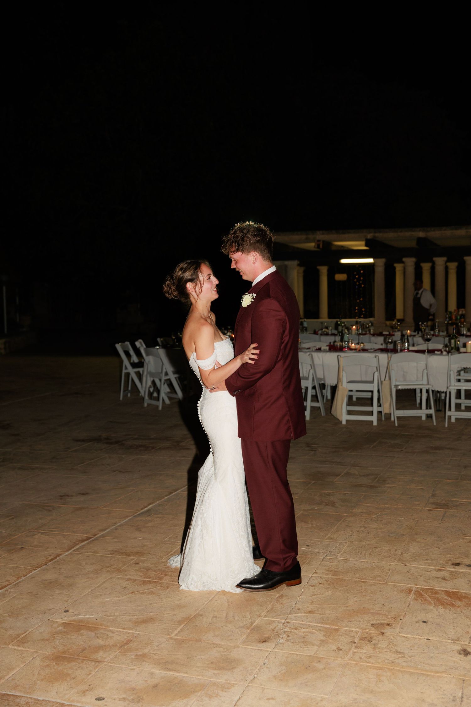 A newlywed couple shares their first dance on an outdoor patio during an evening reception.