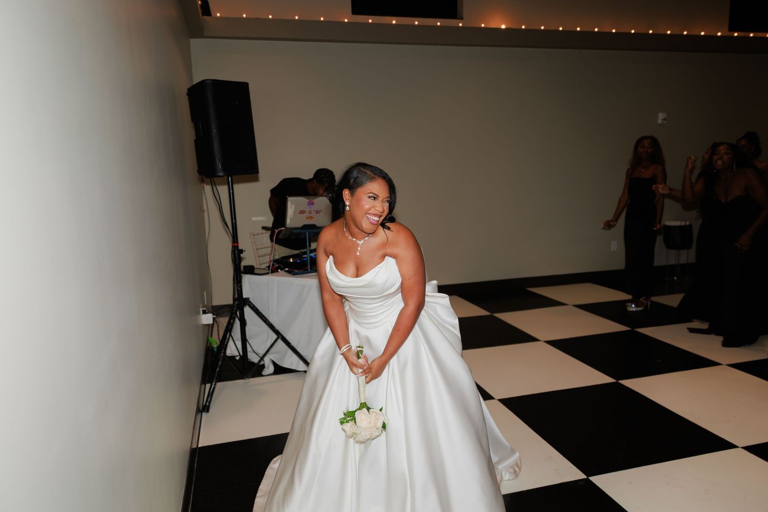 A bride in a classic white ball gown poses on a black and white checkered floor.
