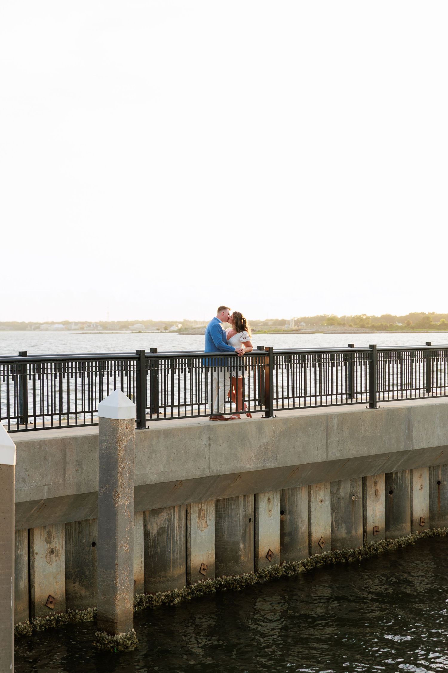 Couple sharing a tender moment on a waterfront pier with a scenic ocean view in the background.