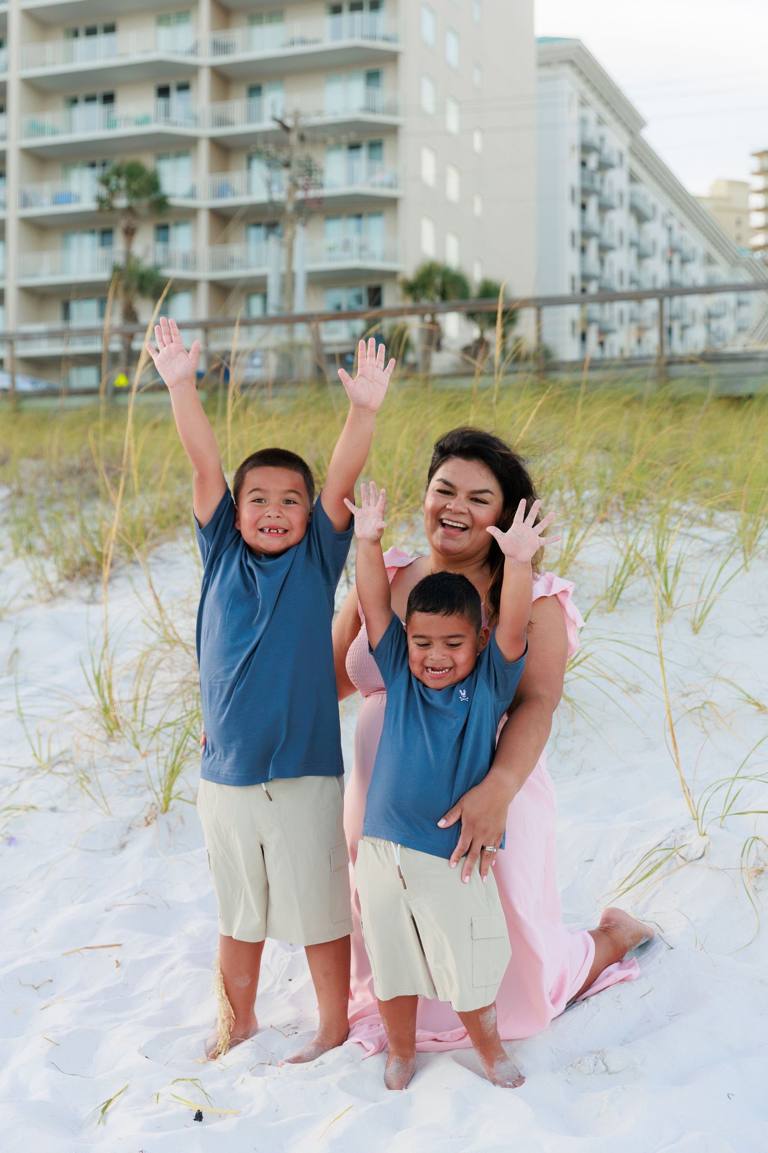 Playful family photoshoot on a beach with sand dunes and coastal buildings in the distance.