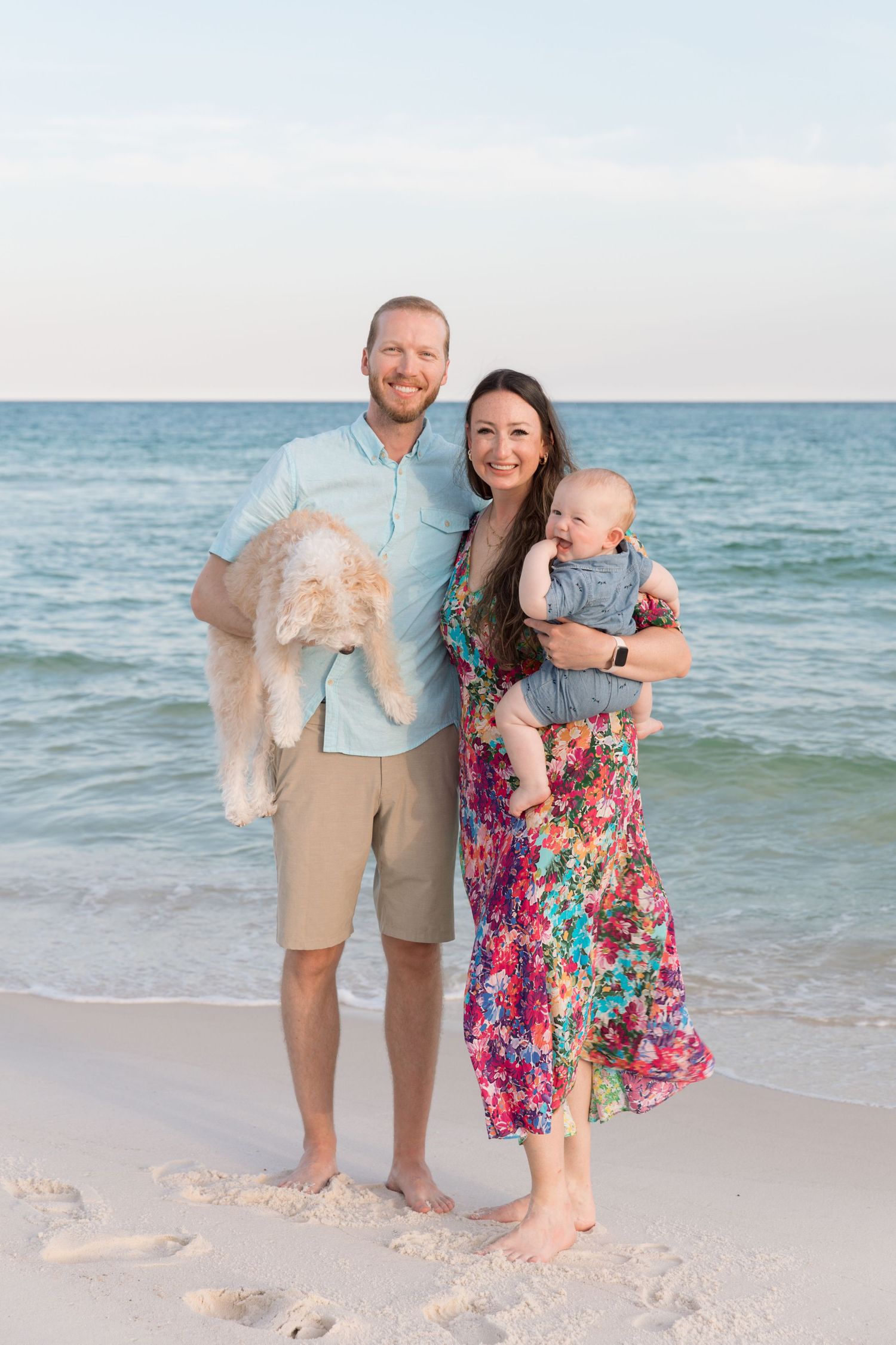 A family poses together on a white sandy beach with the blue ocean waves in the background.