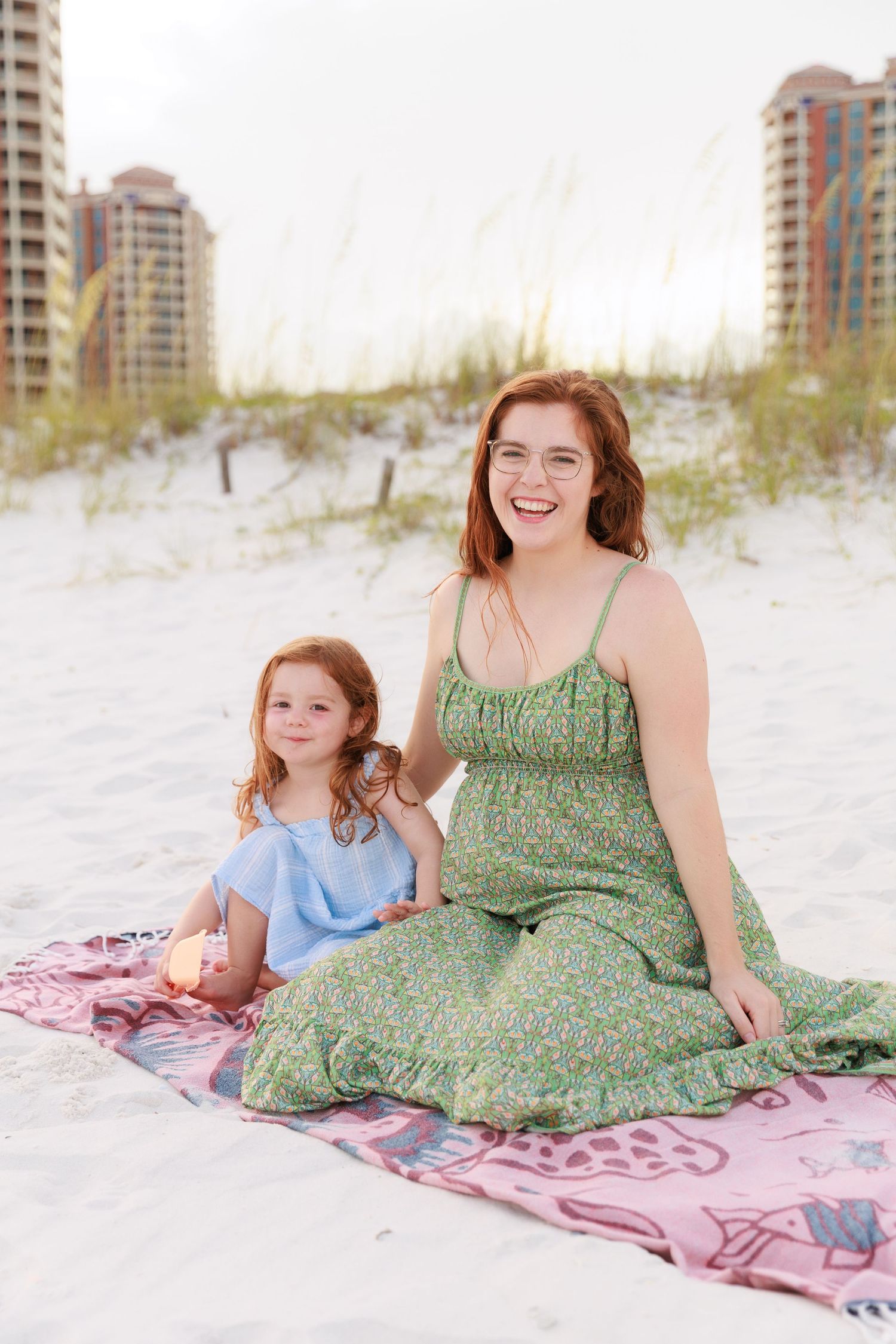 A relaxing beach scene with people lounging on a pink blanket against a backdrop of coastal condominiums.