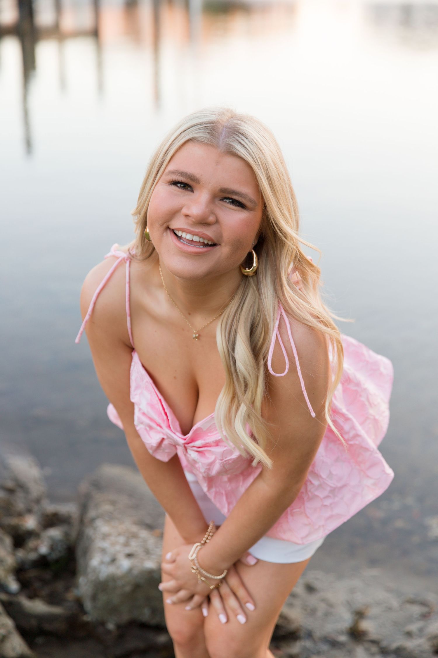 A person in a pink dress poses playfully on a beach at sunset.