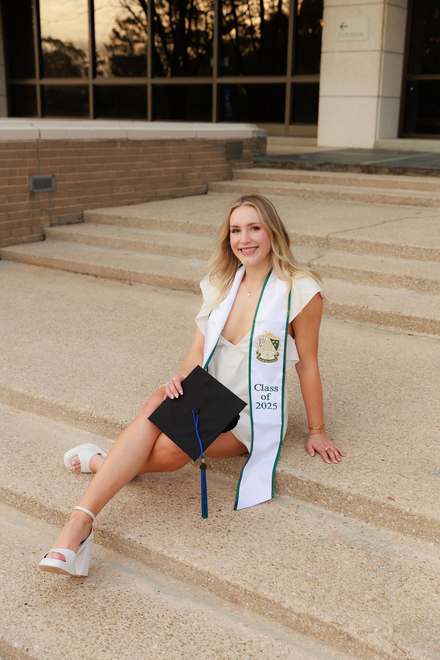 Young woman in graduation cap and Class of 2025 stole sits on steps, celebrating her academic achievement.