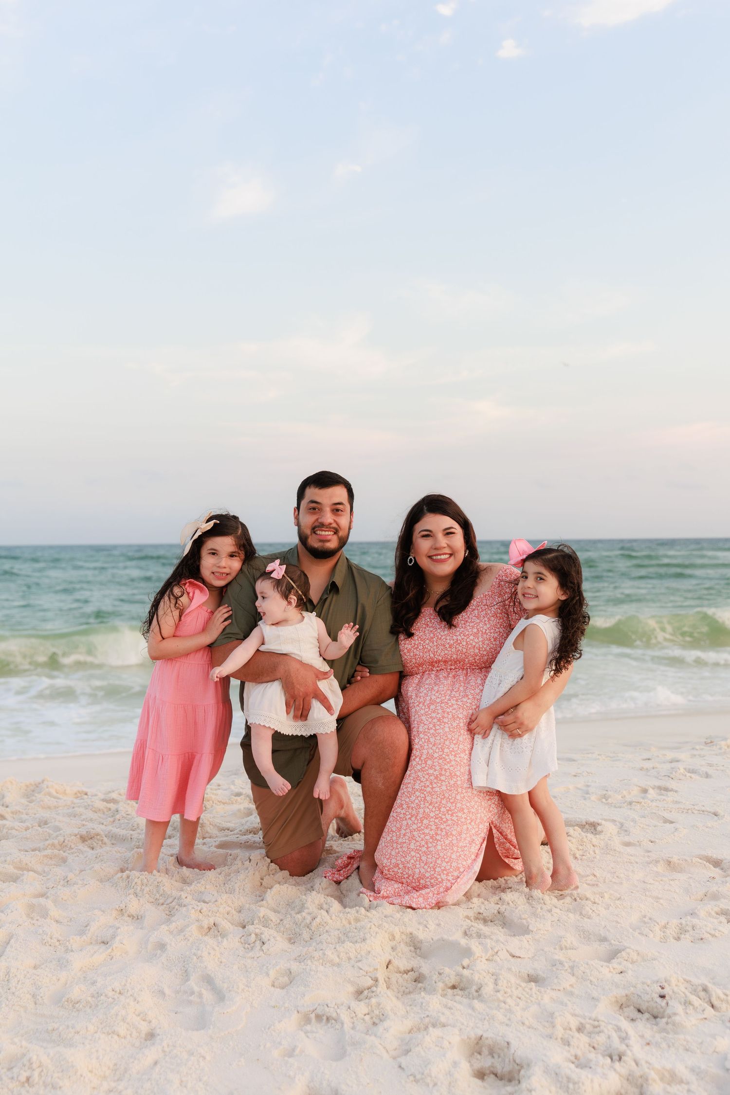 Family of five posing together on a sandy beach with turquoise ocean waves in the background.
