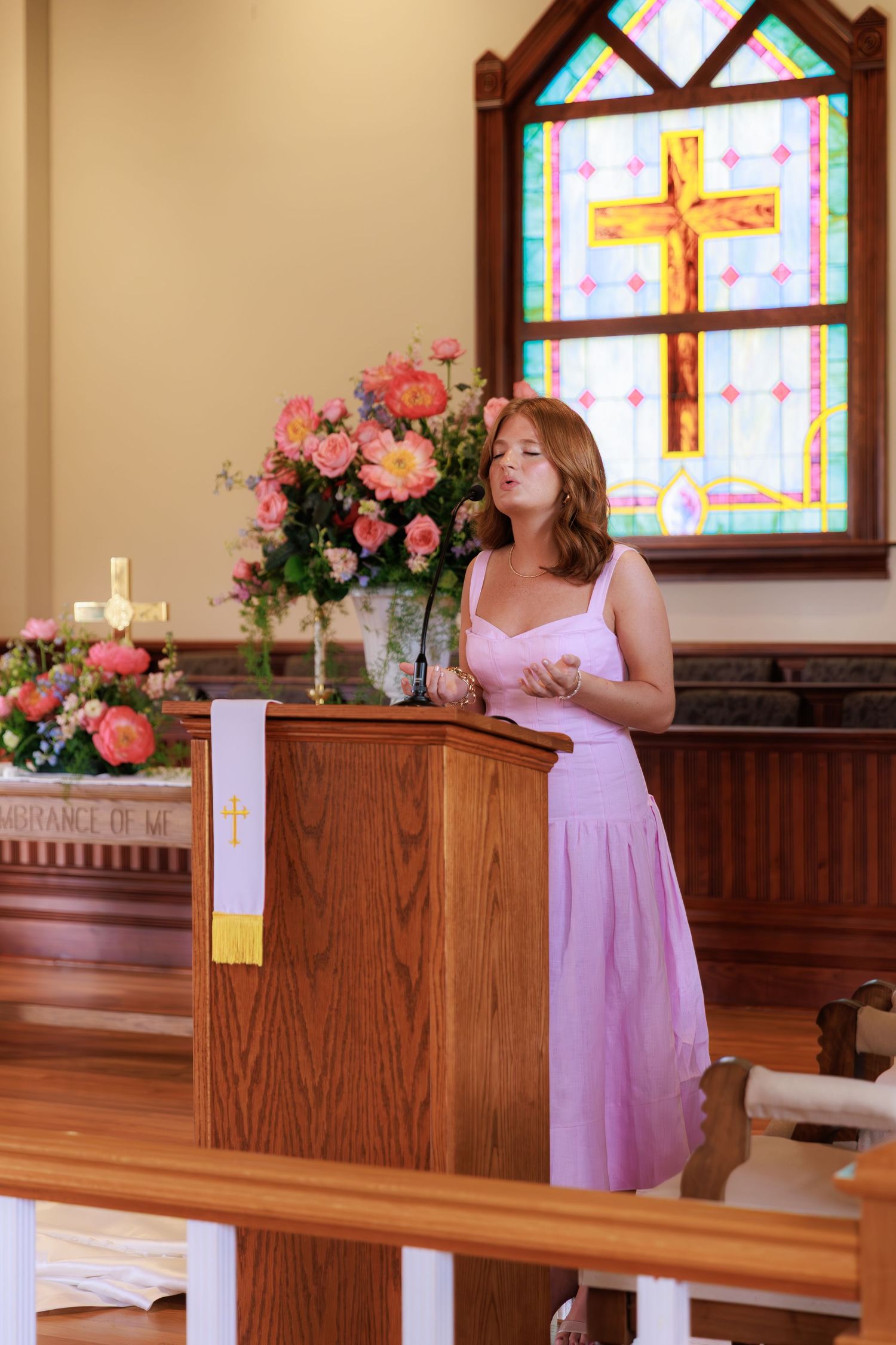 Church altar decorated with pink floral arrangements and stained glass windows for wedding ceremony.