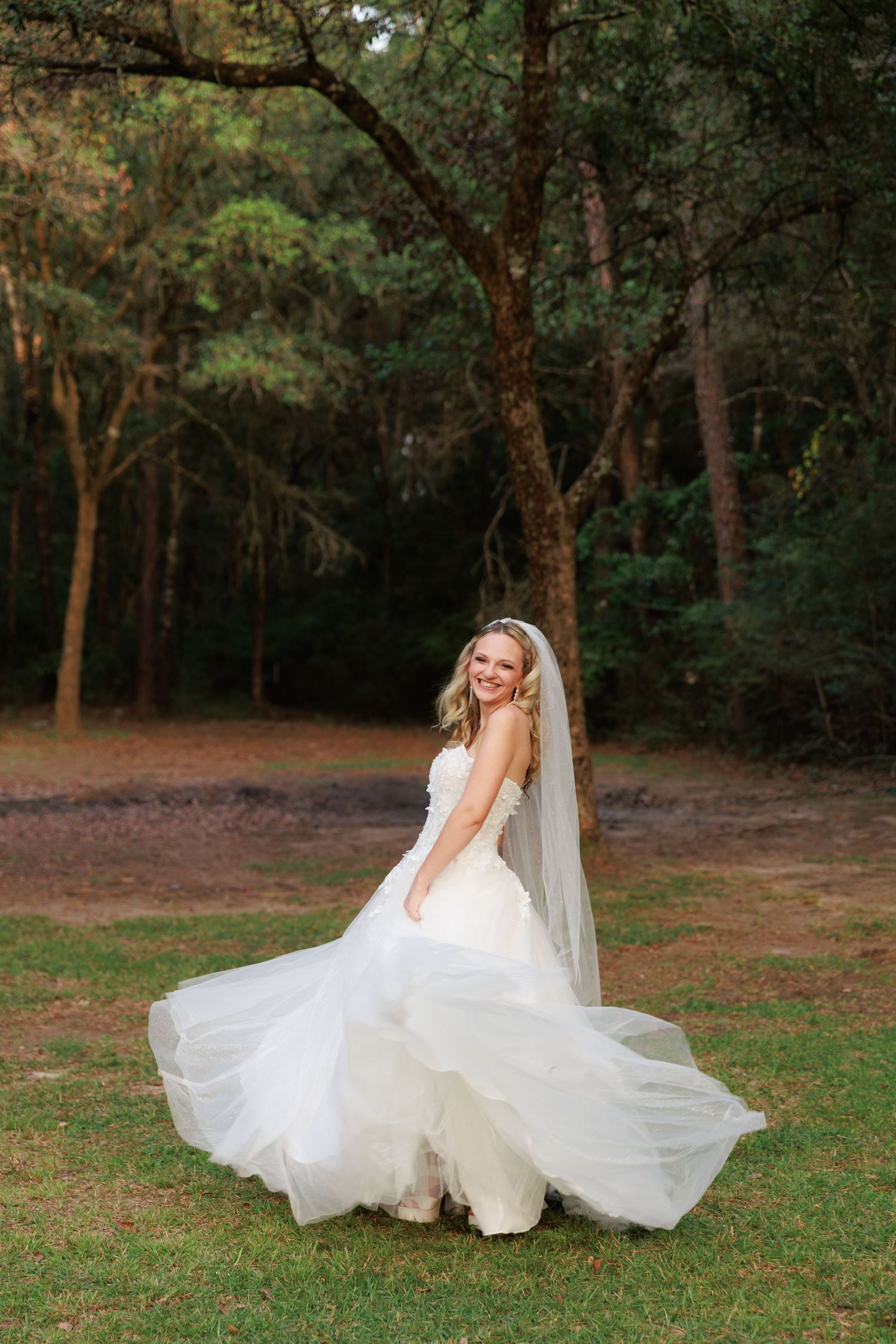 A flowing white wedding dress twirls gracefully in a wooded outdoor setting during a romantic bridal photoshoot.