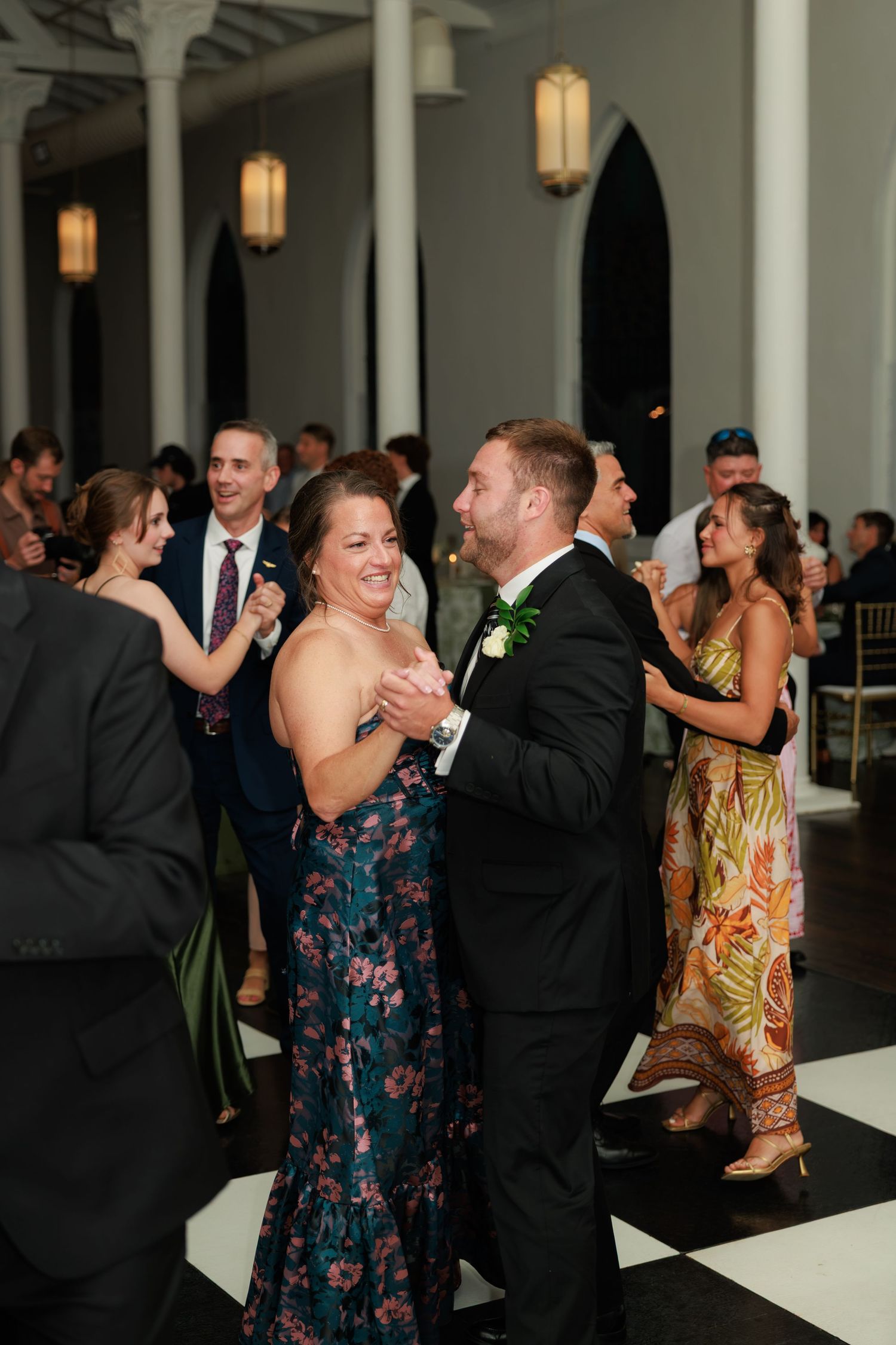 Guests dancing joyfully at a wedding reception in an elegant venue with black and white floors.
