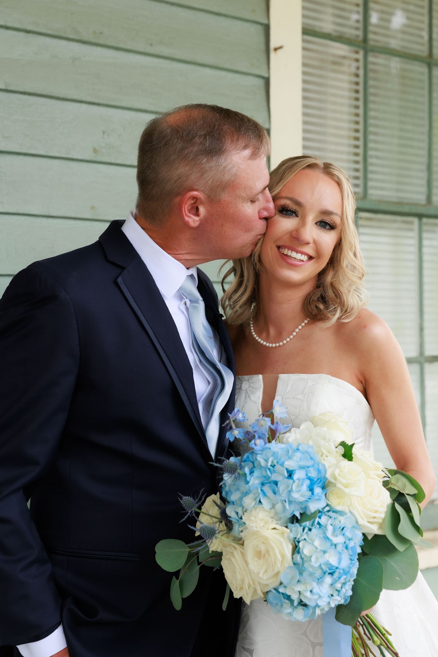 Sweet moment shared between couple with blue and white hydrangea bouquet on vintage porch.
