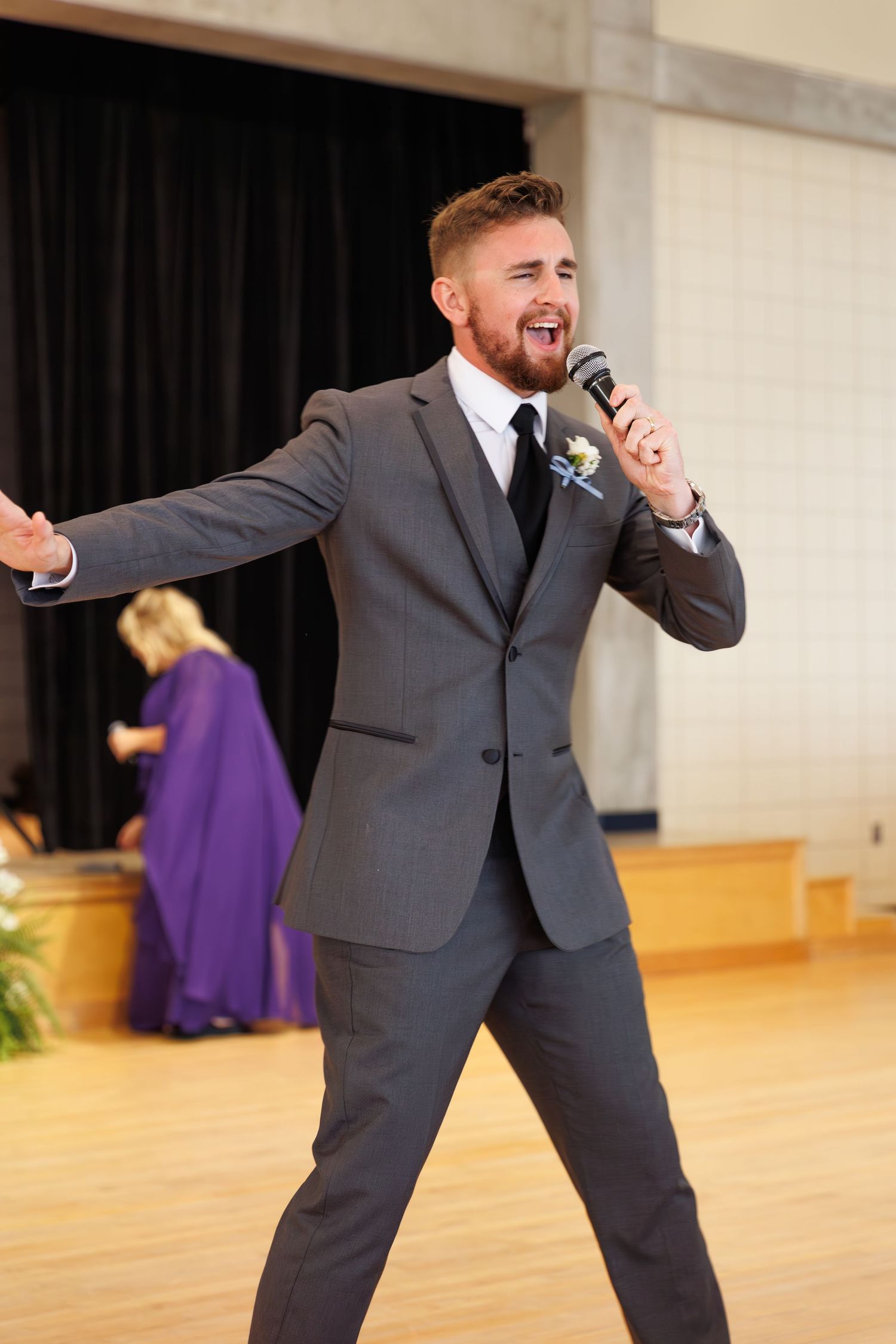 A performer in a grey suit enthusiastically sings into a microphone during a wedding reception performance.