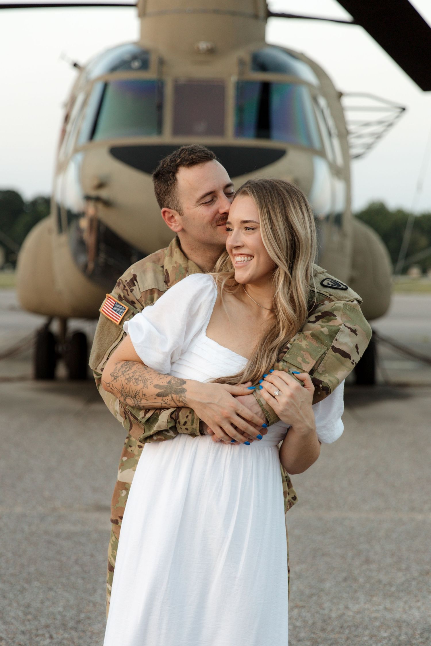 Couple embraces in front of military helicopter during photoshoot.