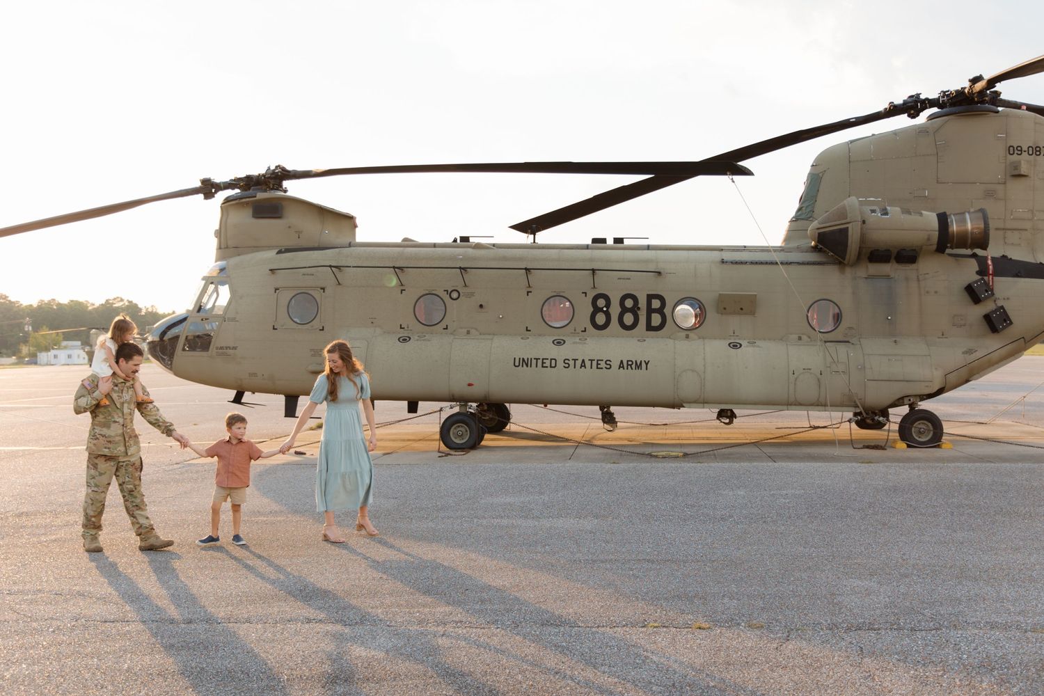 Military family walking together near a Chinook helicopter on an airfield.