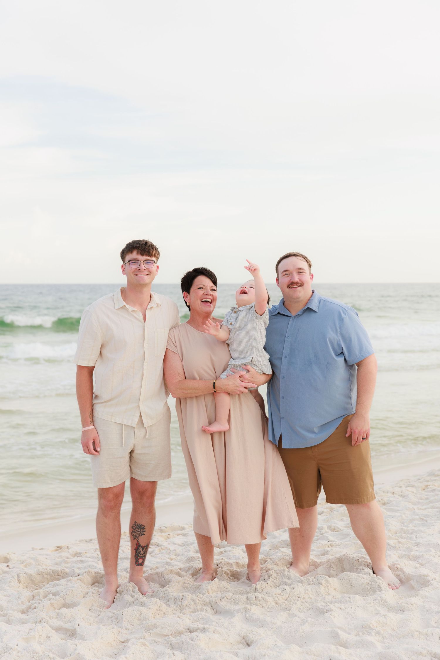 Extended family poses together for a casual portrait on a white sandy beach with ocean waves behind them.