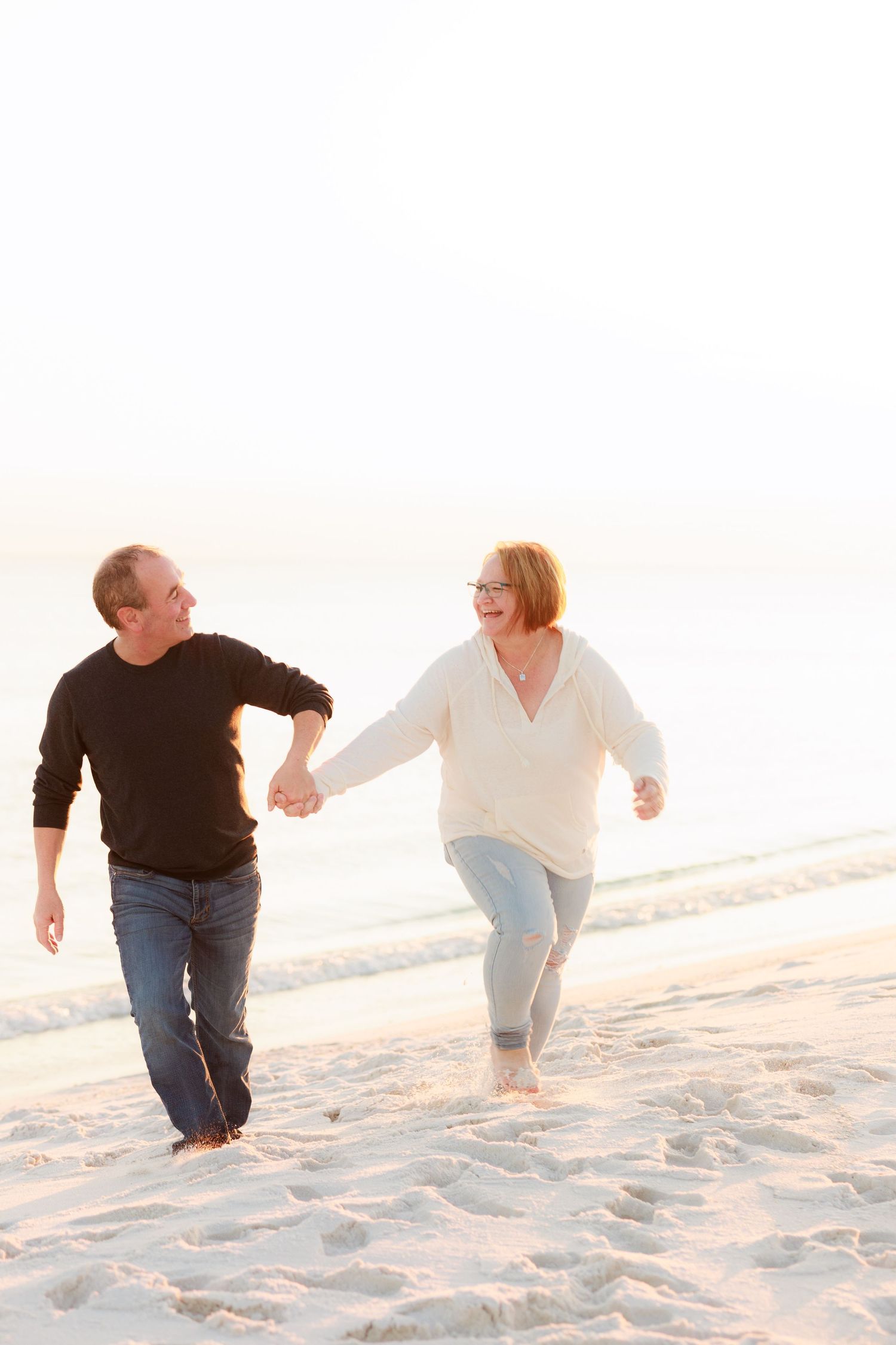 Family members holding hands while walking together on a white sandy beach at sunset.