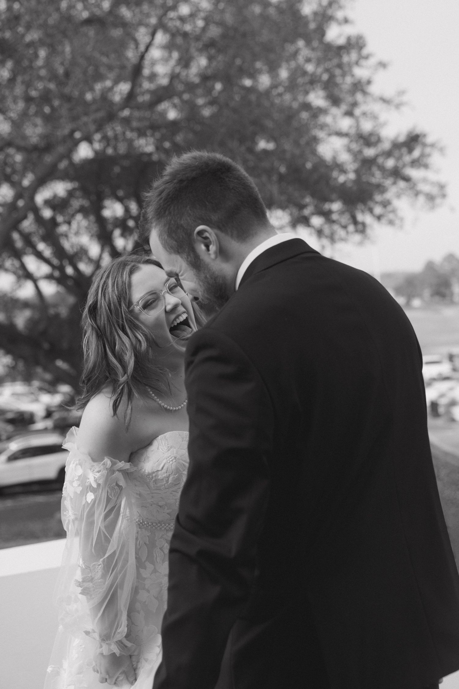 Black and white photo of a laughing bride in a strapless gown sharing a joyful moment with a groom in a suit.