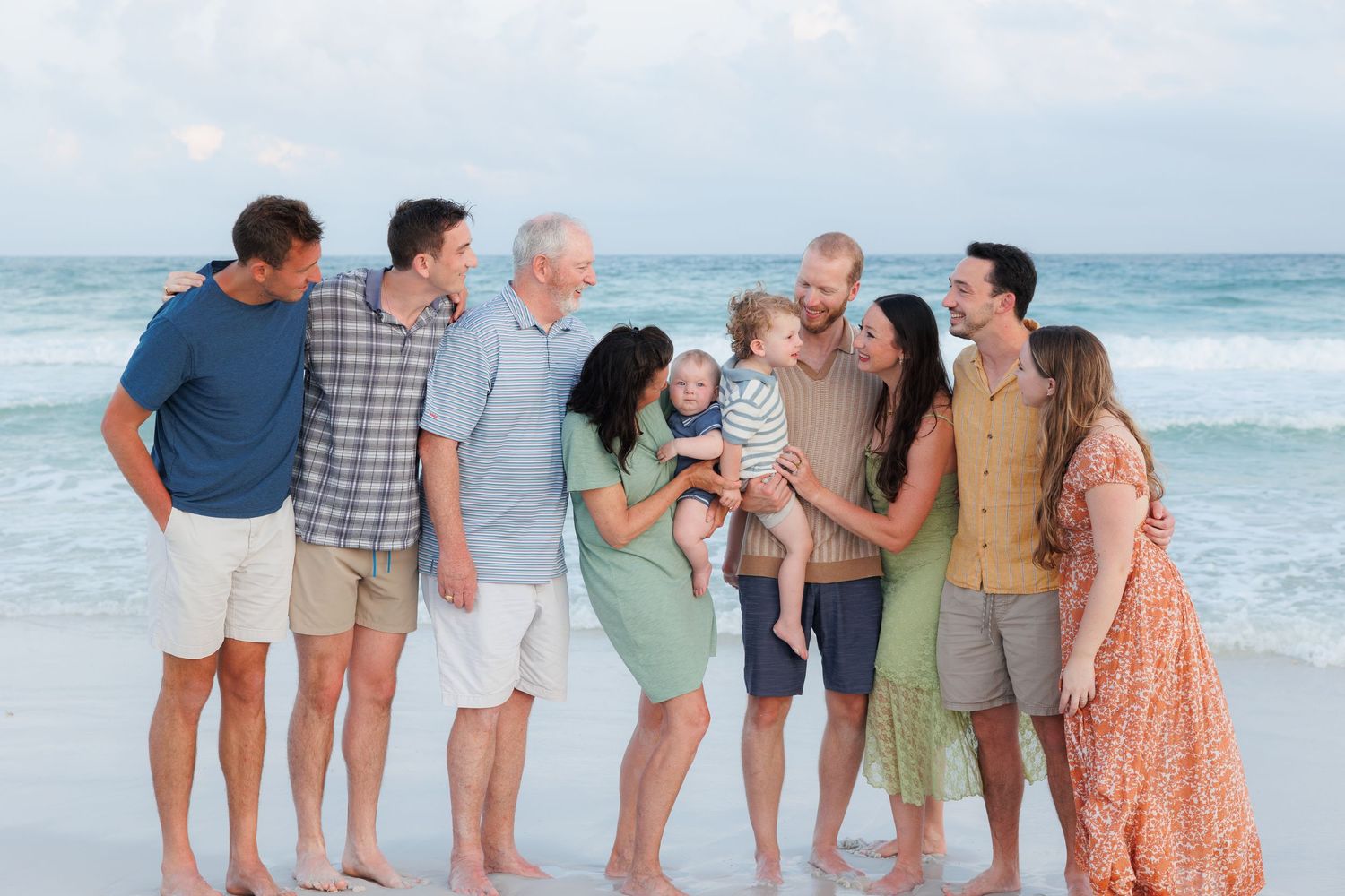 Multi-generational family smiling together on a sandy beach with ocean waves in the background.