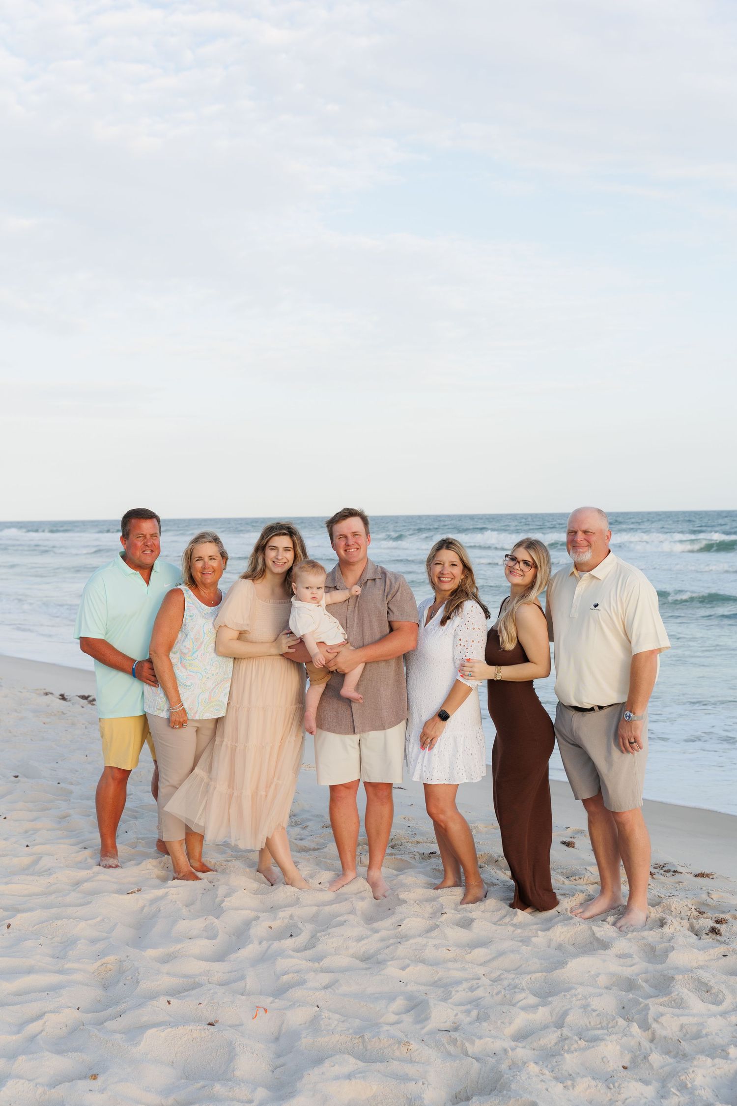 Multi-generational family of seven poses together on a white sand beach with ocean waves in the background.