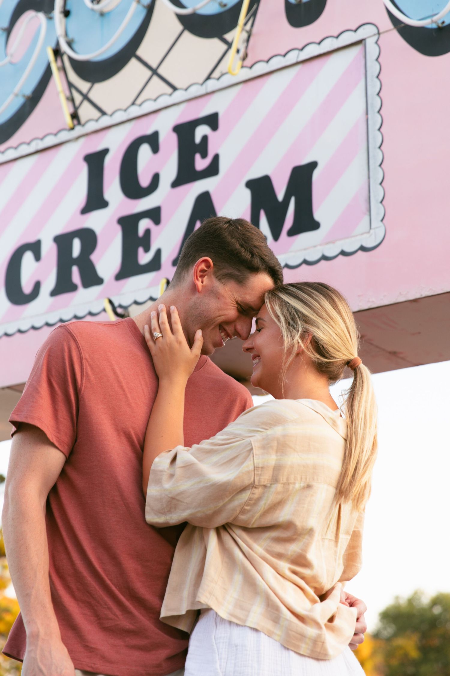 A romantic moment captured in front of a vintage ice cream parlor sign at sunset.