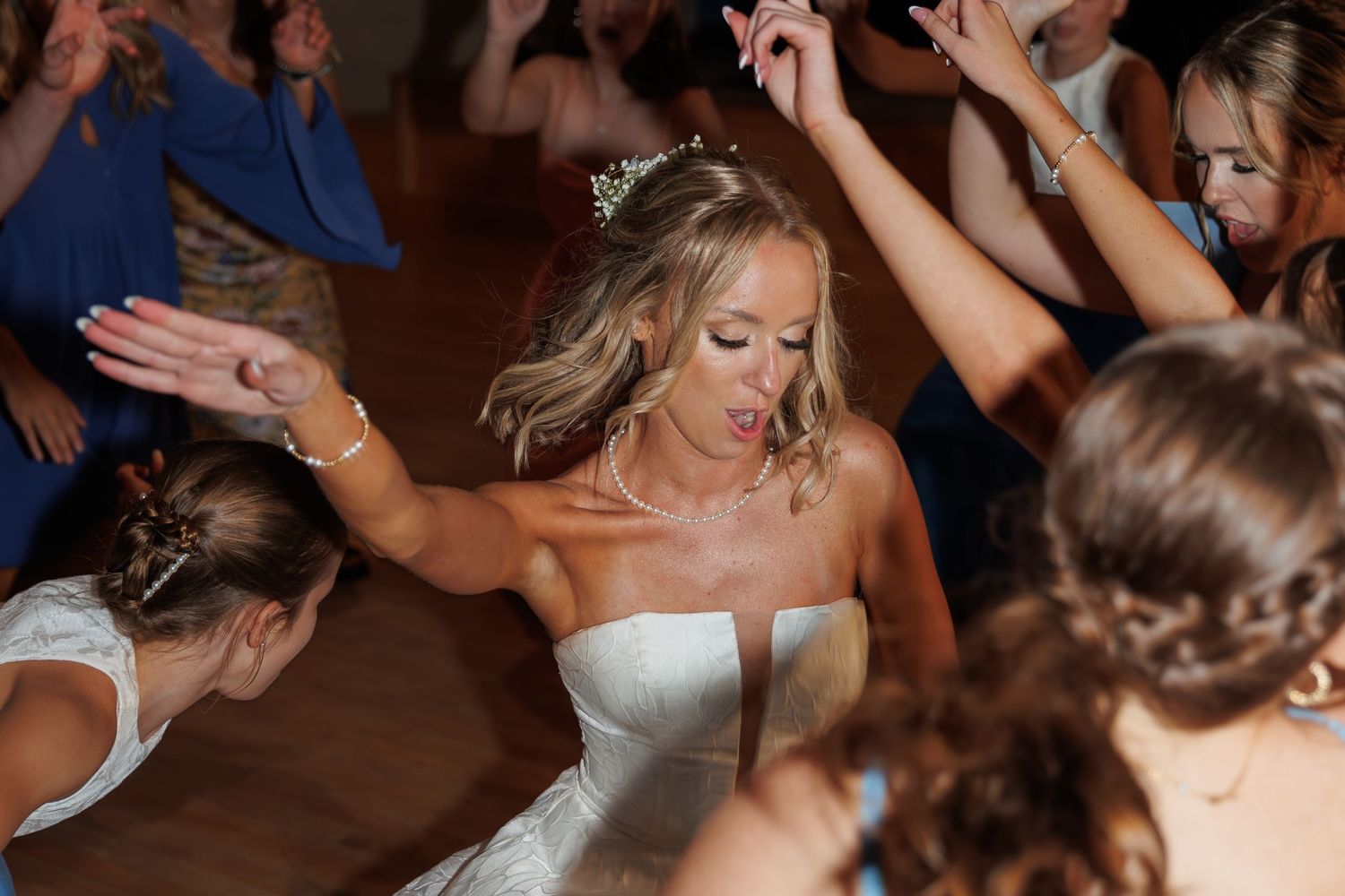 A bride and her wedding guests dancing with raised arms on the dance floor.