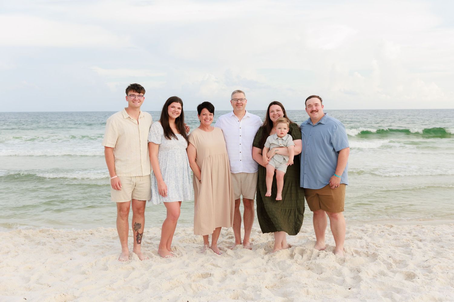 A group of people in coordinated neutral outfits standing together on a sunny beach.