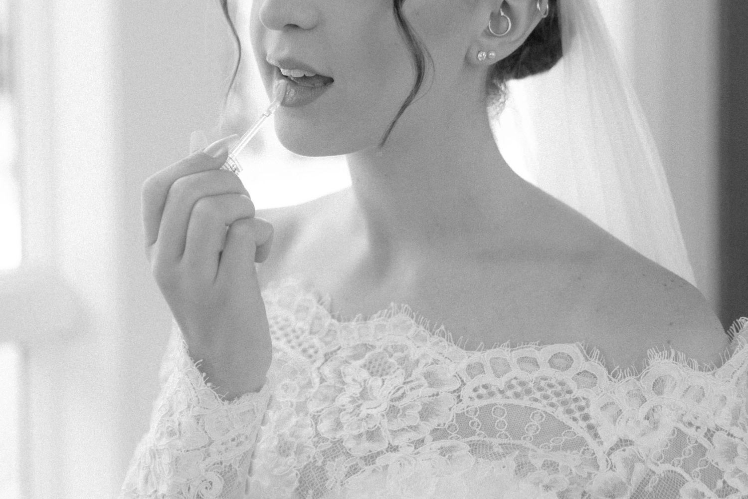 Black and white portrait of bride in off-shoulder lace wedding dress with delicate veil and soft natural lighting.