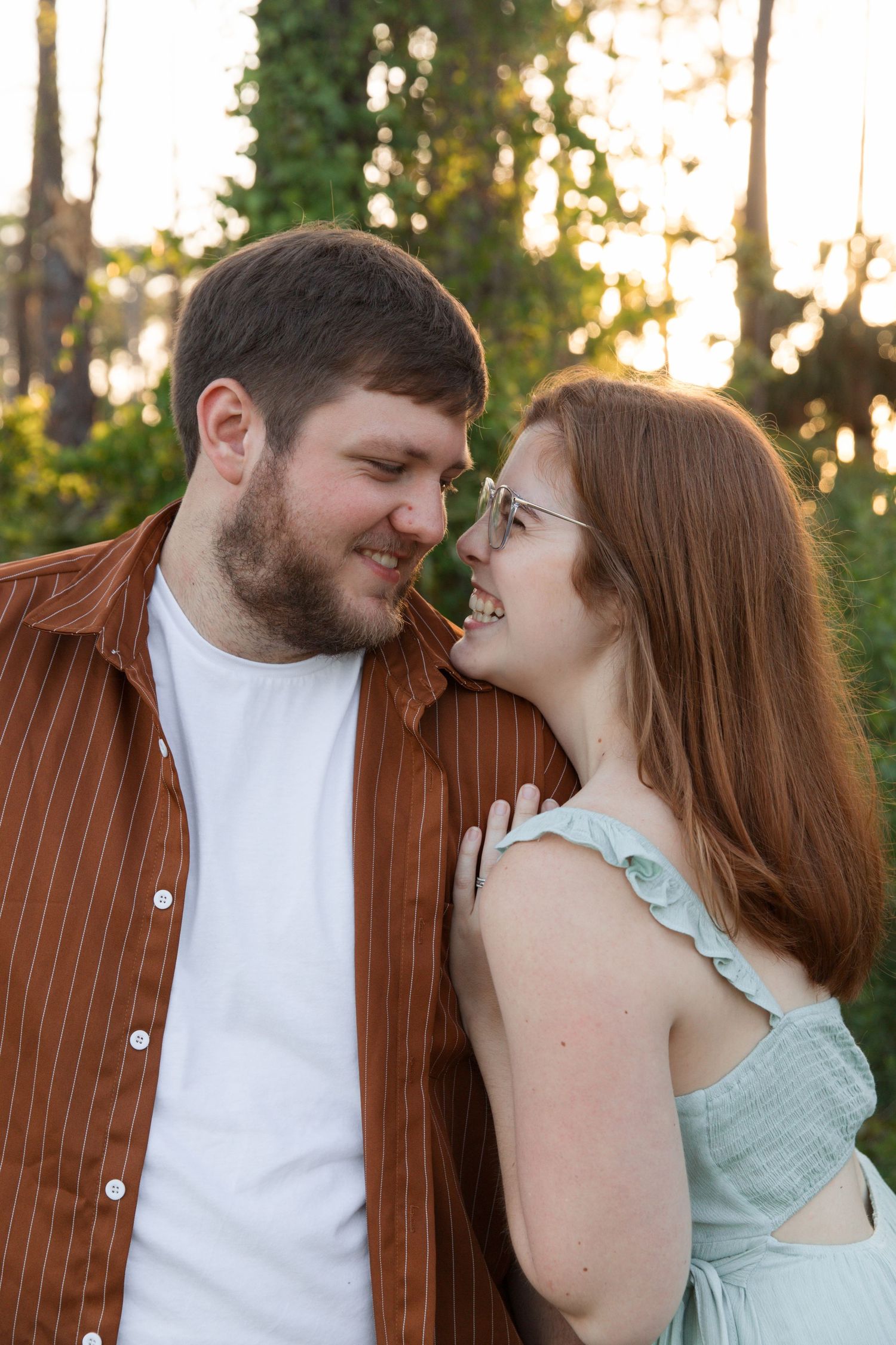 A couple shares an intimate moment outdoors with warm sunset lighting filtering through trees in the background.