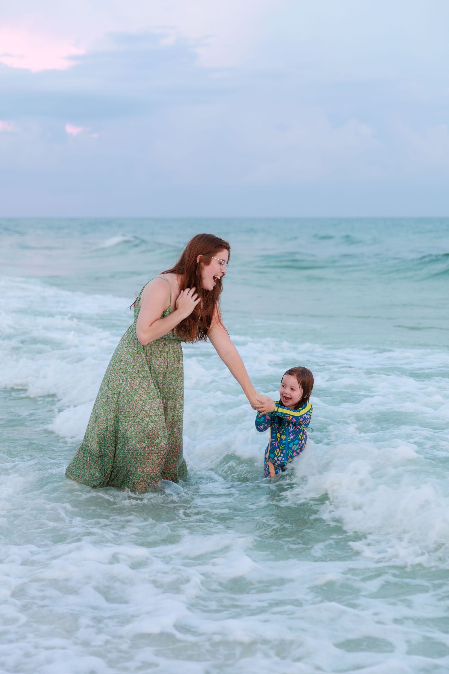 A playful moment captured in turquoise ocean waves as two figures splash and interact in the shallow water.