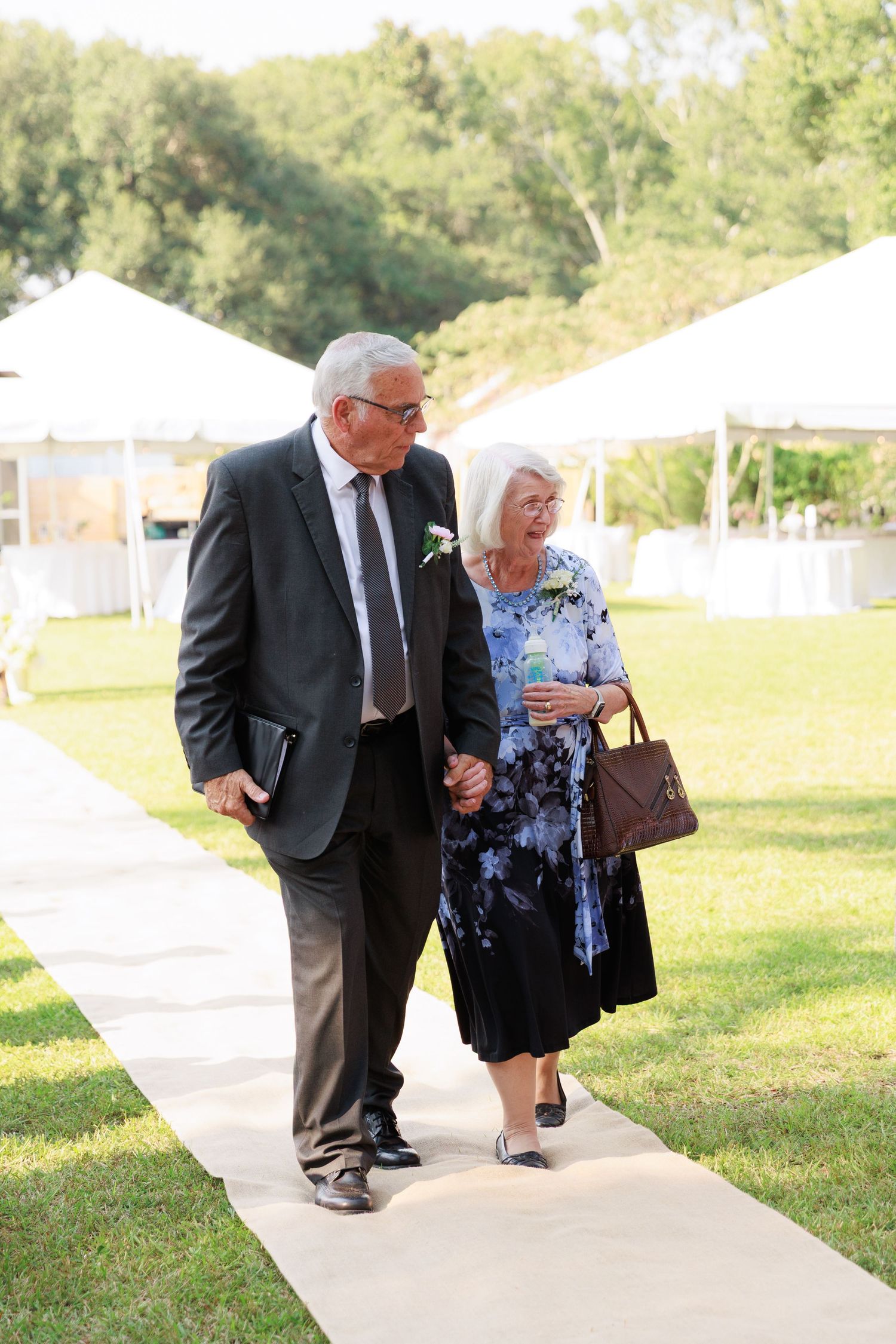 People walking along a concrete path with white tents and green grass on a sunny day.