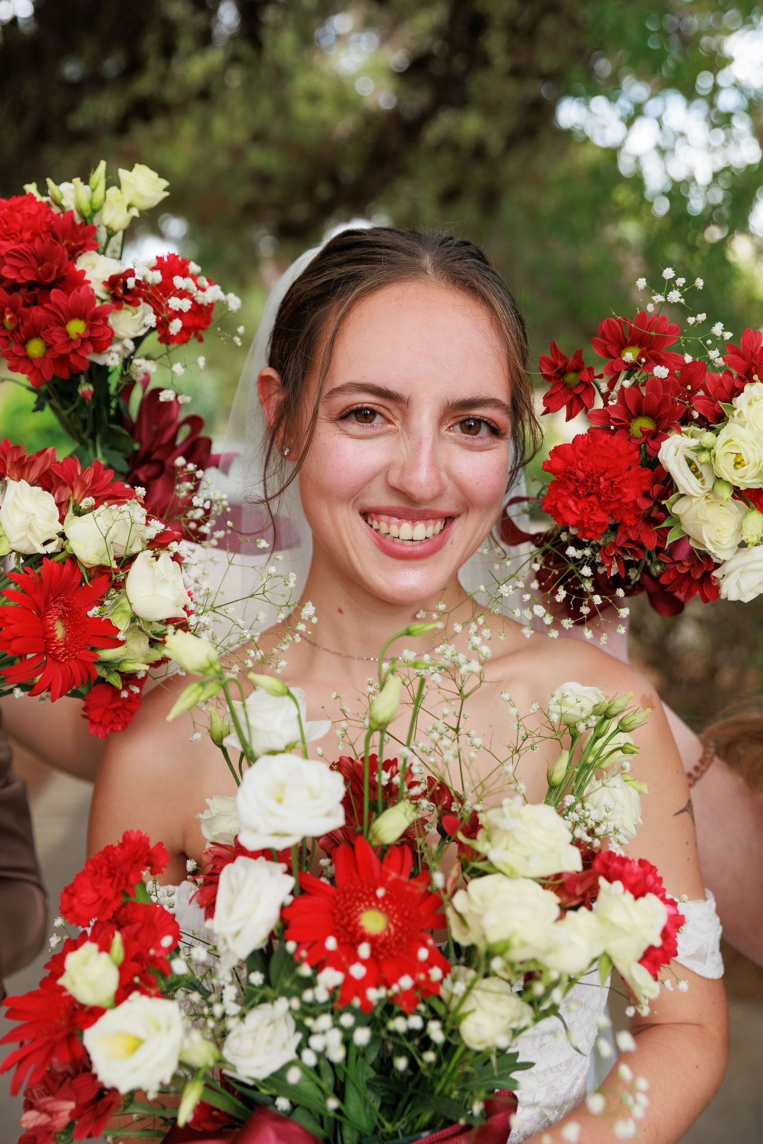 Beautiful bridal portrait with vibrant red and white floral arrangements against a natural outdoor background.