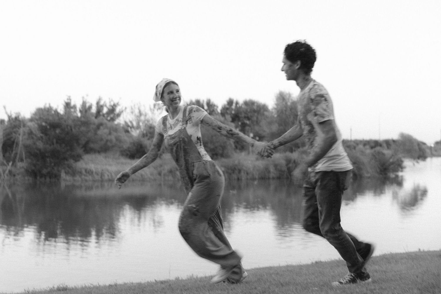 Two people dance and laugh together by a serene lake in a joyful black and white moment.