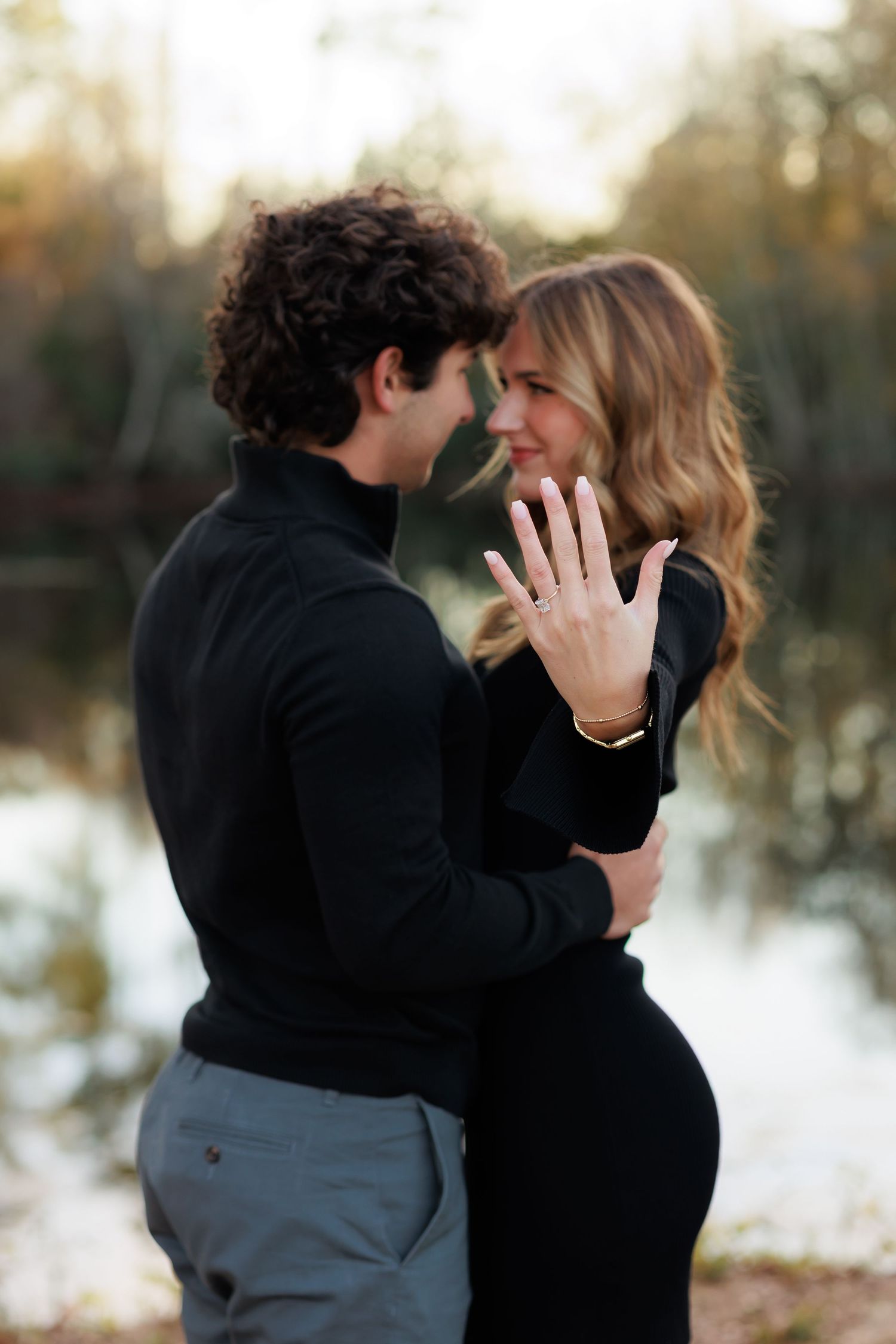 A romantic couple embraces in a snowy winter setting during an intimate outdoor photoshoot at sunset.