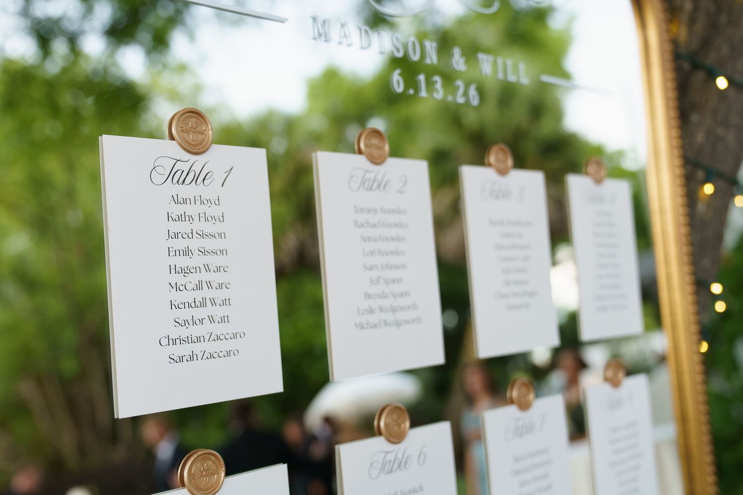 Elegant wedding seating chart displayed on a gold-framed mirror with white cards and wax seals for Madison and Will.