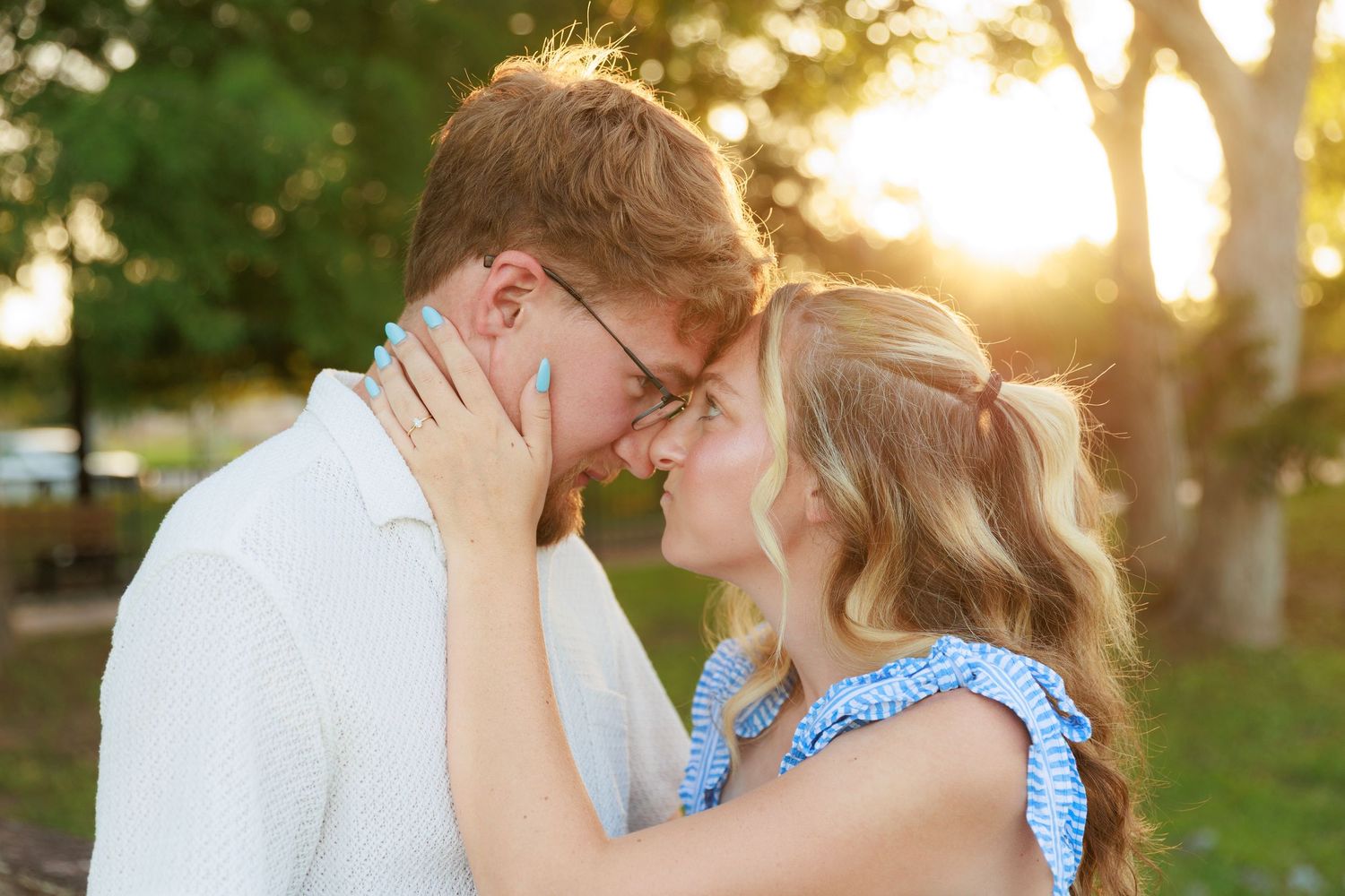 Young couple sharing a romantic forehead touch at golden hour in a sunlit park setting.