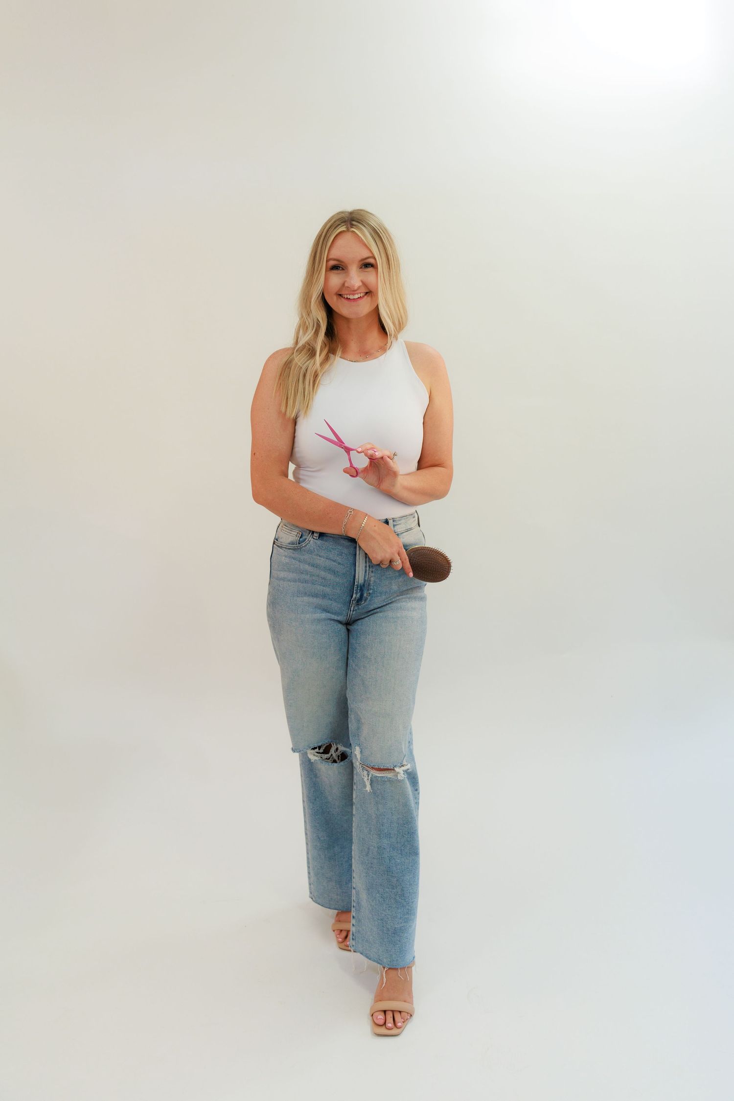 Woman in casual white tank top and ripped jeans poses in studio setting.